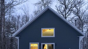 A two-story house with a dark exterior, a visible interior with a kitchen, and a snowy landscape. - Paddle, Play & Relax: Home w/ Pioneer Lake Access! (Conover)