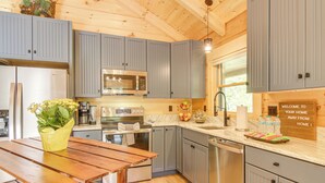 A modern kitchen with grey cabinets, stainless steel appliances, and a wooden dining table. - Amazing Waterfall! New Scenic Black Mtn Log Cabin (Black Mountain)