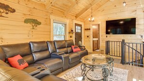 A cozy log cabin interior with a leather sofa, a glass coffee table, and a mounted TV. - Amazing Waterfall! New Scenic Black Mtn Log Cabin (Black Mountain)