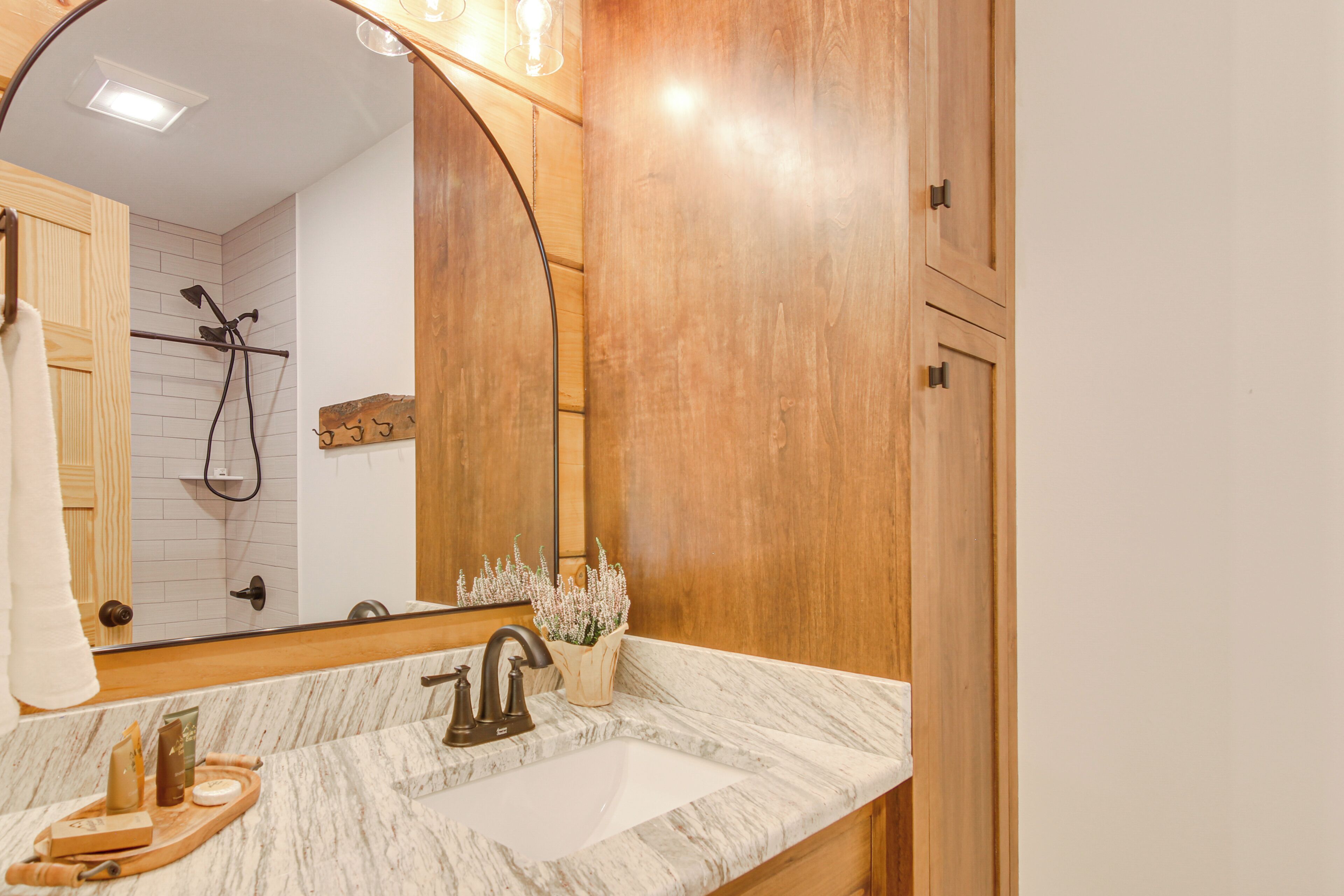 A bathroom with a marble sink, wooden cabinets, a large mirror, and a shower area.
