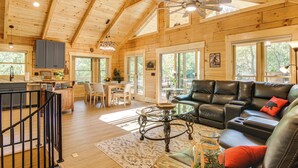 A spacious wooden cabin with a dining area, a living room with leather furniture, and large windows offering views of the outdoors. - Amazing Waterfall! New Scenic Black Mtn Log Cabin (Black Mountain)