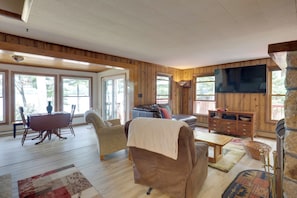 Un salón espacioso con suelo de madera, un sofá, una mesa de comedor con sillas, una chimenea y un televisor montado en la pared.