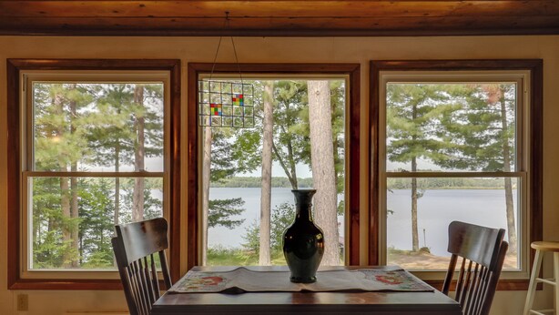 A dining area with a table, chairs, a vase, and a view of a lake through large windows. - Lakefront Family Home w/ Dock, Views: Pet-friendly (Conover)