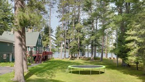 A grassy yard with a trampoline, a house with a green roof, and tall trees. - Lakefront Family Home w/ Dock, Views: Pet-friendly (Conover)