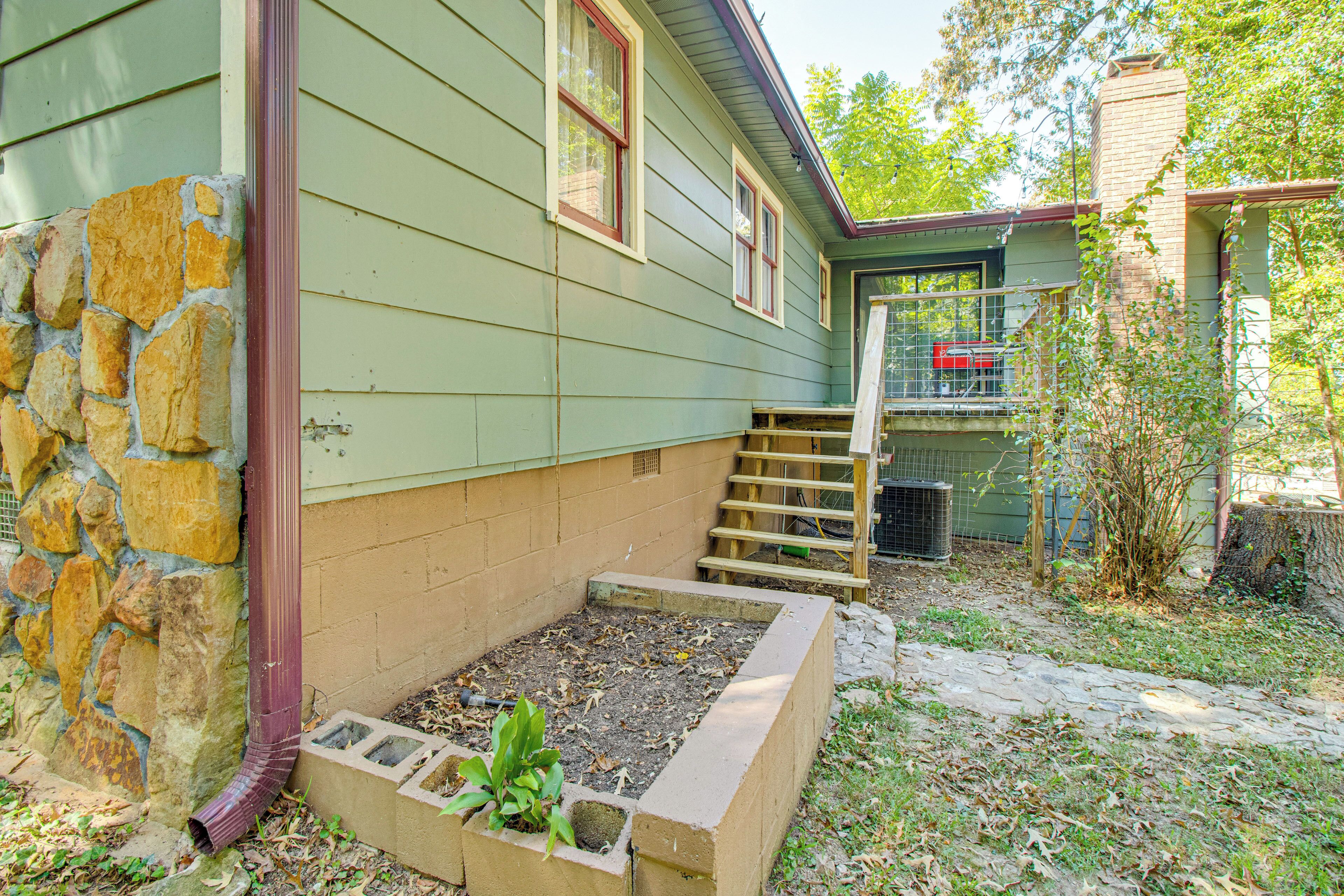A house with a stone foundation, a raised garden bed, and a wooden staircase leading to a covered porch.