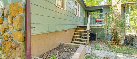 A house with a stone foundation, a raised garden bed, and a wooden staircase leading to a covered porch.