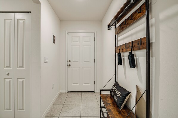 A hallway with a white door, a bench with a 'Welcome' pillow, and a coat rack with jackets. - Tranquil Getaway w/ Spacious Yard in Brooksville! (Brooksville)