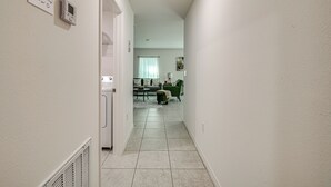En hall som leder till ett vardagsrum med en termostat, ett ventilationsdon och en dörr.