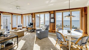 A spacious living area with a large window offering a view of the sea, a ceiling fan, and a dining table with chairs. - Pool & Stunning Water Views: Kent Island Home! (Stevensville)