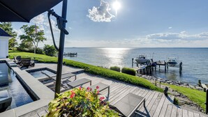 A deck with lounge chairs overlooking a lake, docked boats, and a well-maintained lawn. - Pool & Stunning Water Views: Kent Island Home! (Stevensville)