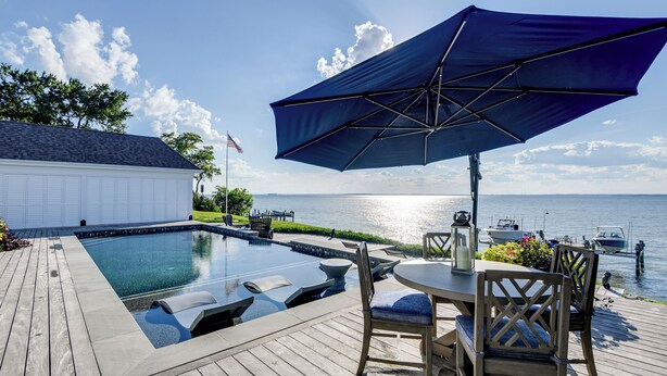 A wooden deck with a pool, outdoor furniture, and a view of the water. - Pool & Stunning Water Views: Kent Island Home! (Stevensville)