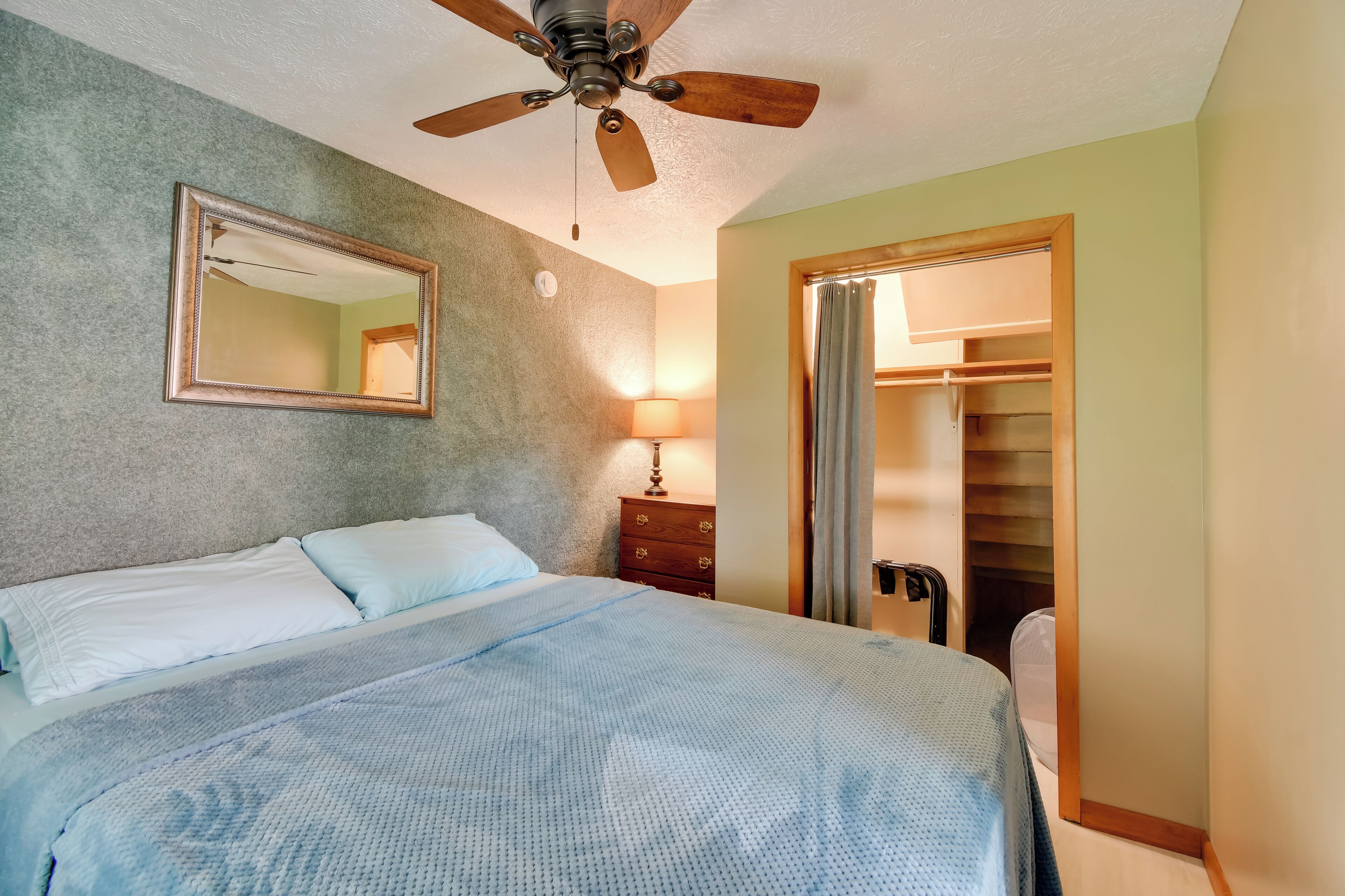 A bedroom with a bed, a ceiling fan, a mirror, a dresser, and a closet.