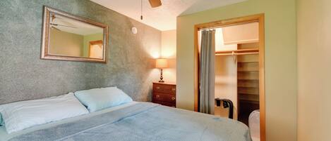 A bedroom with a bed, a ceiling fan, a mirror, a dresser, and a closet.