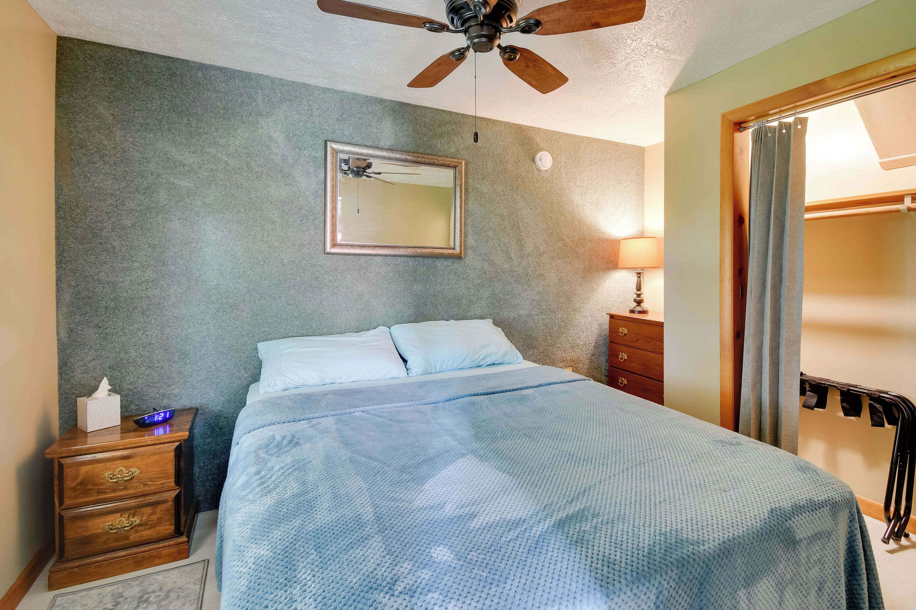 Une chambre à coucher comprenant un lit, une table de chevet, un ventilateur de plafond, un miroir, une lampe et une armoire.