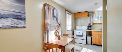 A compact kitchen with wooden cabinets, a dining table with chairs, and a painting of a seascape on the wall.