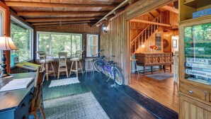 L’intérieur chaleureux d’un chalet avec un plafond en bois, un coin repas avec des chaises, un vélo et une bibliothèque remplie de livres.