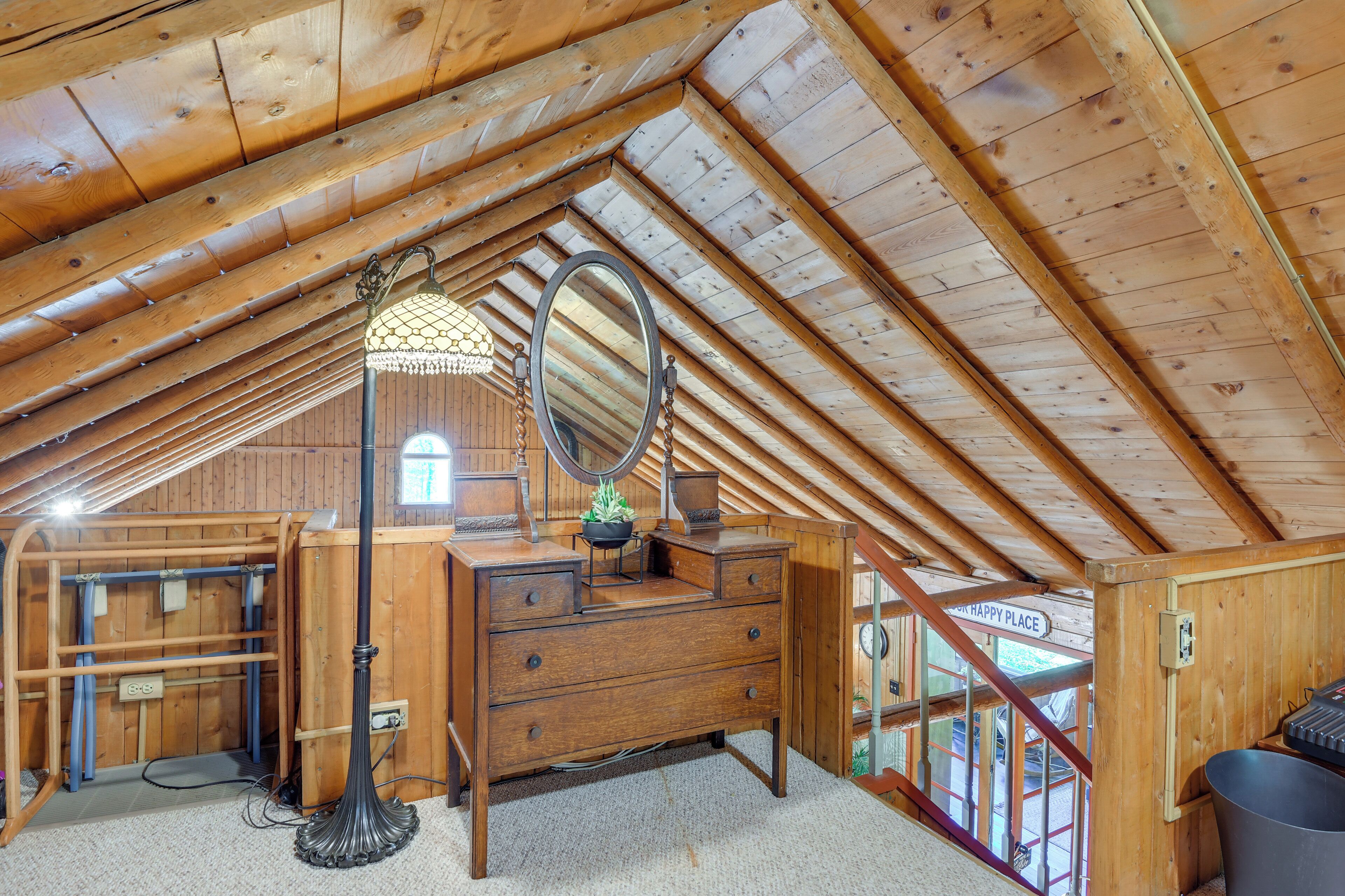 A wooden attic bedroom with a dresser, a mirror, and a hanging lamp.