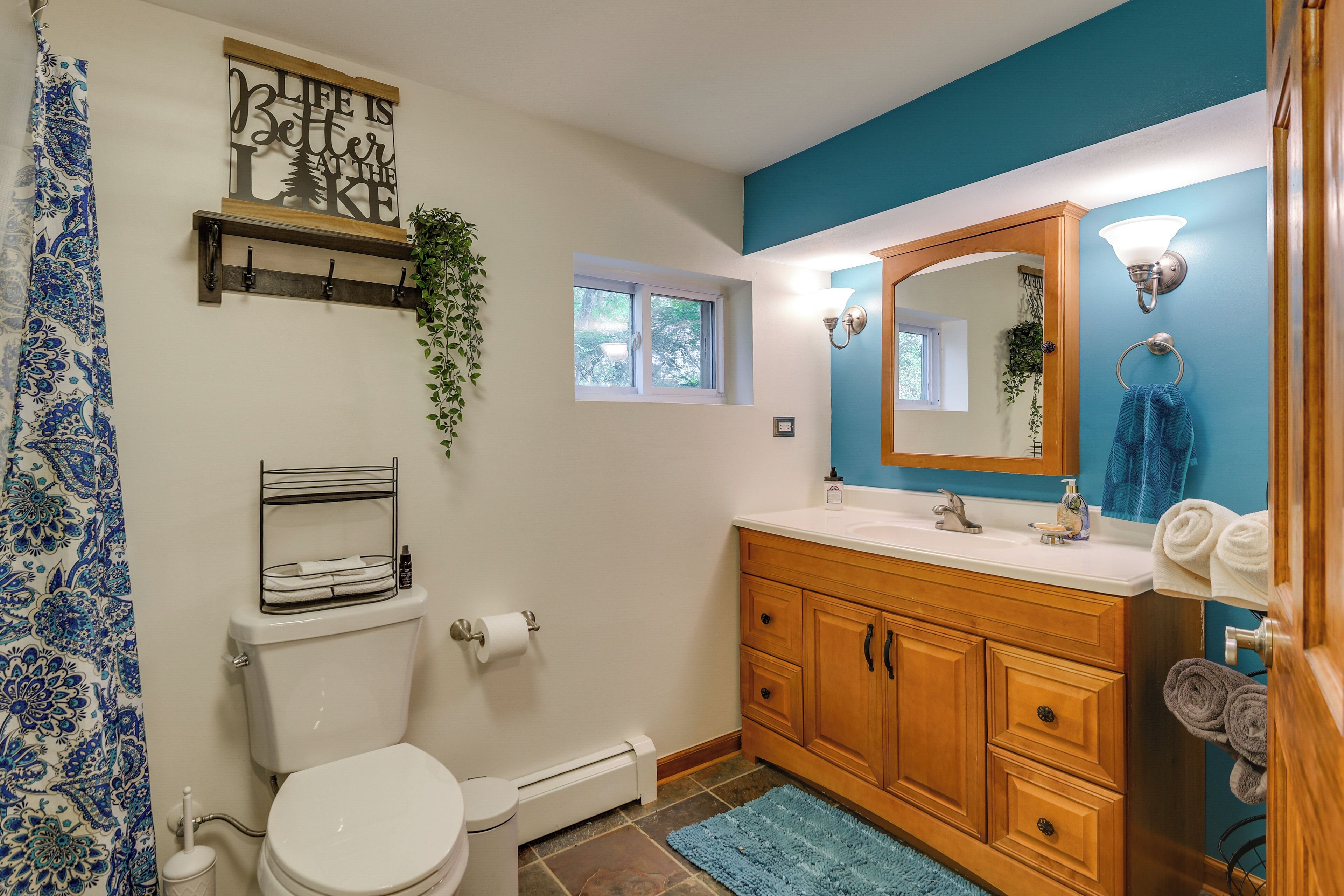 Un baño con inodoro, lavabo, armarios de madera, un espejo, toallero y ventana.