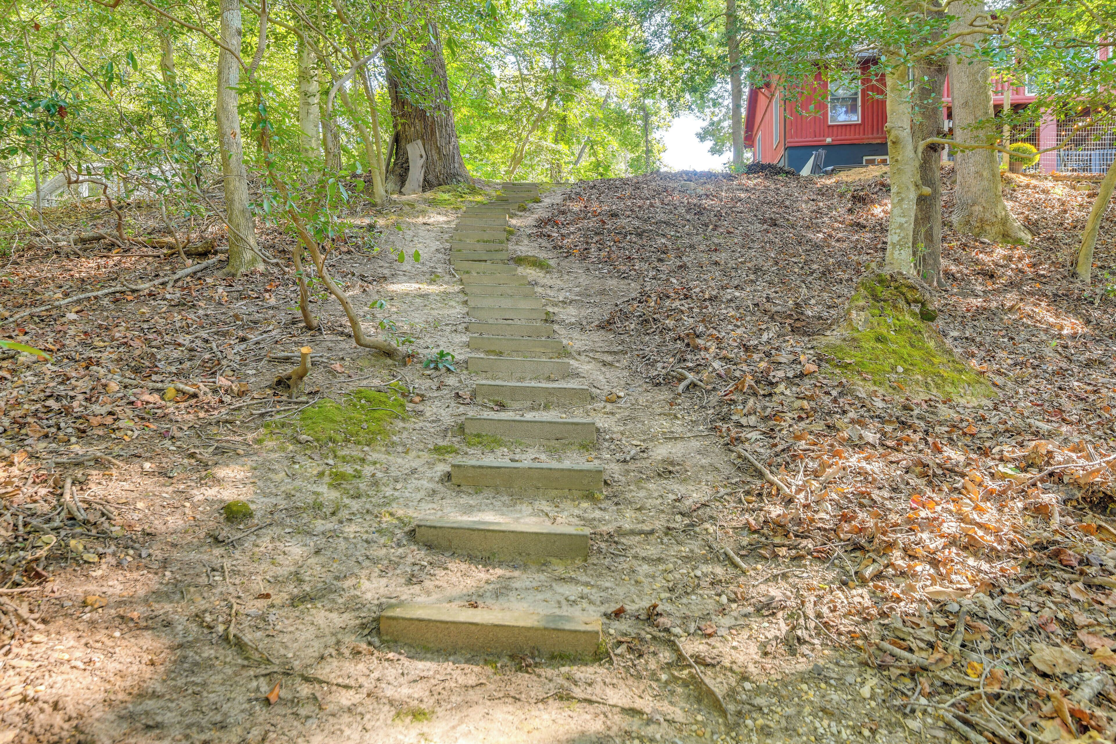Una escalera de piedra que sube una colina en un área boscosa, con un edificio rojo al fondo.