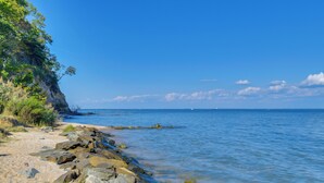 Une plage rocheuse avec une eau d’un bleu limpide et un bateau qui se trouve au loin.