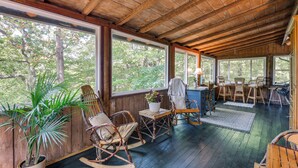 Une terrasse en bois avec des fauteuils à bascule, une table agrémentée d’une plante et un coin repas avec des chaises et une table.