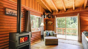 A cozy cabin interior with a wood-burning stove, a sofa, and a window overlooking a forest.