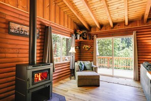 A cozy cabin interior with a wood-burning stove, a sofa, and a window overlooking a forest. - Sonora Hideaway Lake Access & Mountain Charm (Sonora)