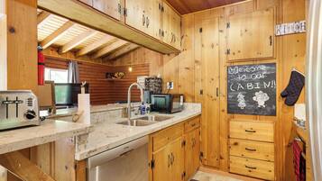 A wooden cabin kitchen with a toaster, sink, microwave, and a chalkboard sign.