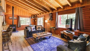 A cozy log cabin interior with a wooden ceiling, a fireplace, a sofa, a coffee table, and a television. - Community Lake Access: Peaceful Cabin in Sonora! (Sonora)
