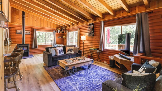 A cozy log cabin interior with a wooden ceiling, a fireplace, a sofa, a coffee table, and a television. - Community Lake Access: Peaceful Cabin in Sonora! (Sonora)