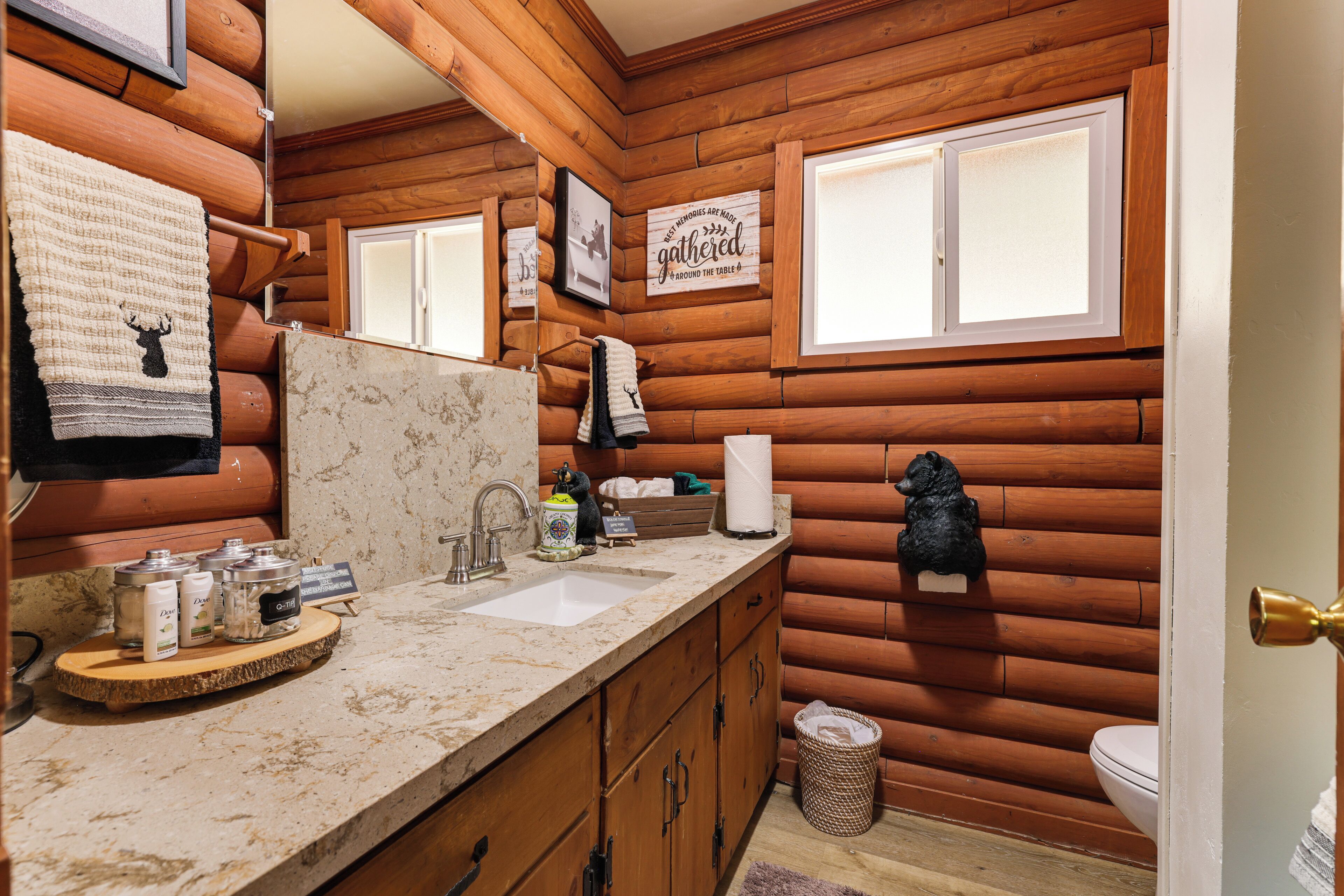 Une salle de bain de style rustique, aménagée comme une cabane, avec des murs en bois, un lavabo doté d’articles de toilette et un miroir.