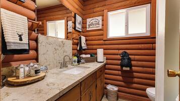 Une salle de bain de style rustique, aménagée comme une cabane, avec des murs en bois, un lavabo doté d’articles de toilette et un miroir.