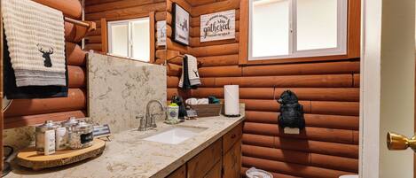 Un baño de estilo rústico tipo cabaña, con paredes de madera, un lavabo con artículos de aseo y un espejo.