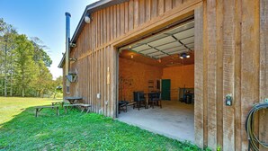 A wooden building with an open garage door, a picnic table, and a covered outdoor area. - Ohio Cabin on 23 Acres: Fish, Hunt & Explore! (Lower Salem)