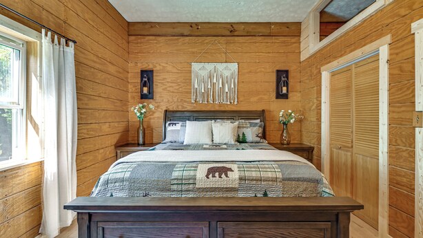 A wooden-paneled bedroom with a bed, nightstands, a dresser, and a window with curtains. - Ohio Cabin on 23 Acres: Fish, Hunt & Explore! (Lower Salem)