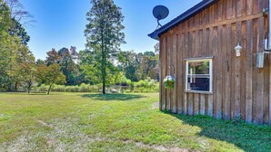 A wooden cabin with a satellite dish, a window with hanging plants, and a view of a pond and trees. - Ohio Cabin on 23 Acres: Fish, Hunt & Explore! (Lower Salem)
