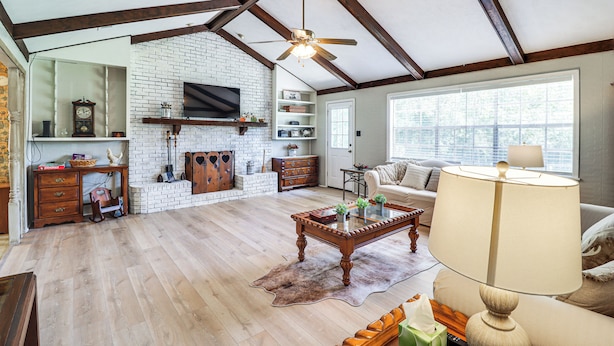 A spacious living room with a wooden ceiling, a fireplace, a television mounted on the wall, and a large window providing natural light. - Rural Retreat: Cypress Lake By Roosevelt St Park (Morton)