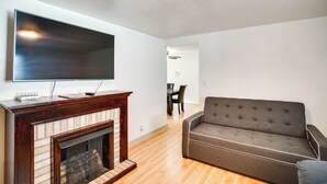 Una sala de estar con una televisión de pantalla plana sobre una chimenea, un sofá gris y un comedor al fondo.