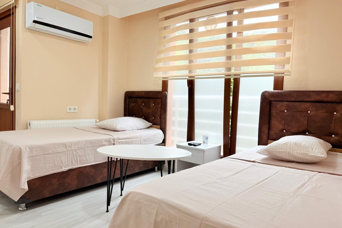 A hotel room with two beds, a small table, and a window with blinds.