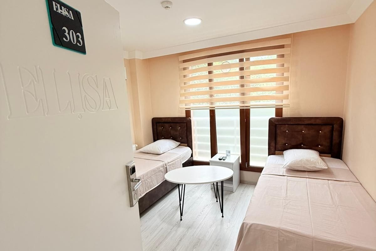 Habitación de hotel con dos camas, una mesita redonda y una ventana con persianas.