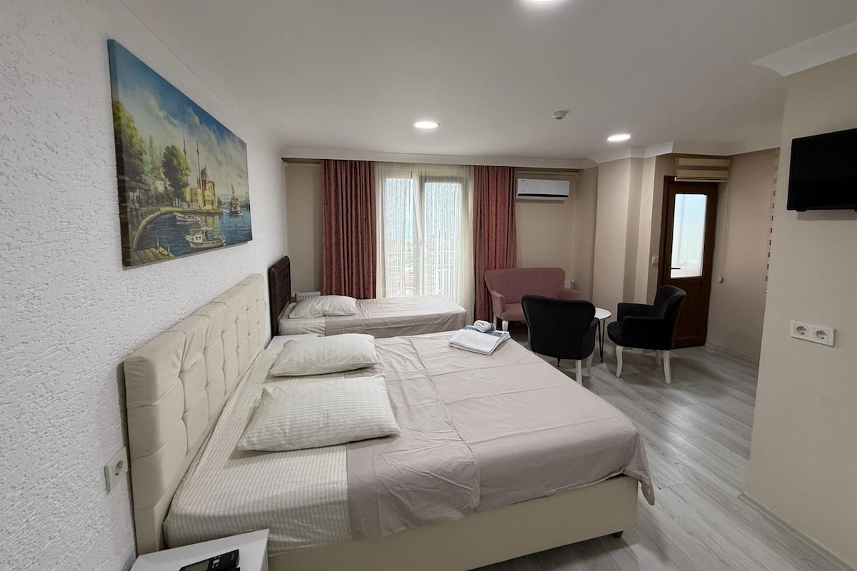 A hotel room with two beds, a desk, a chair, and a painting of a canal scene.
