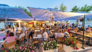An outdoor dining area with tables and chairs, umbrellas, and potted plants. - Adria Holiday - Villaggio San Francesco (Caorle)