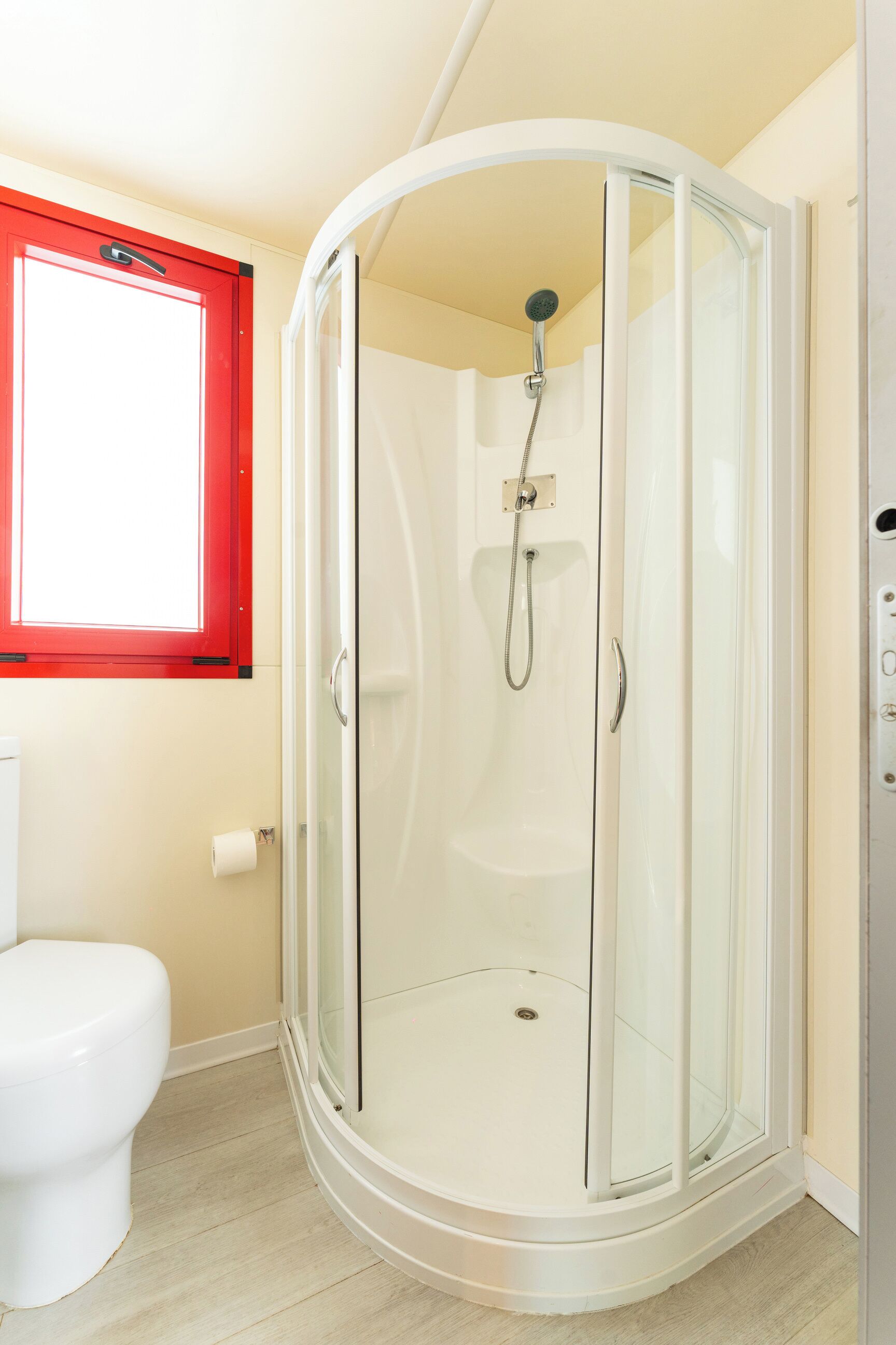 A modern bathroom with a glass-enclosed shower, a white toilet, and a red-framed window.