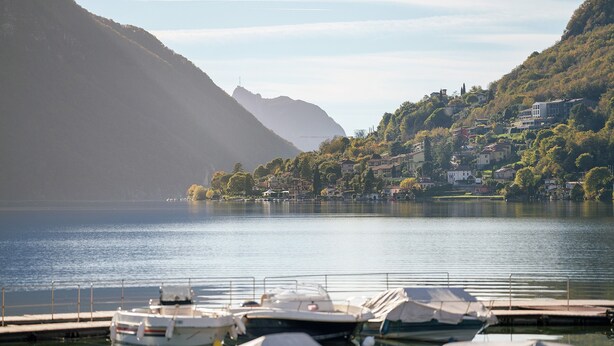 Un lac où sont amarrés des bateaux, une montagne en arrière-plan et une colline parsemée de bâtiments.