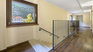 Un couloir doté d’un plancher en bois, d’un escalier en verre et d’une fenêtre donnant sur un immeuble et des arbres.