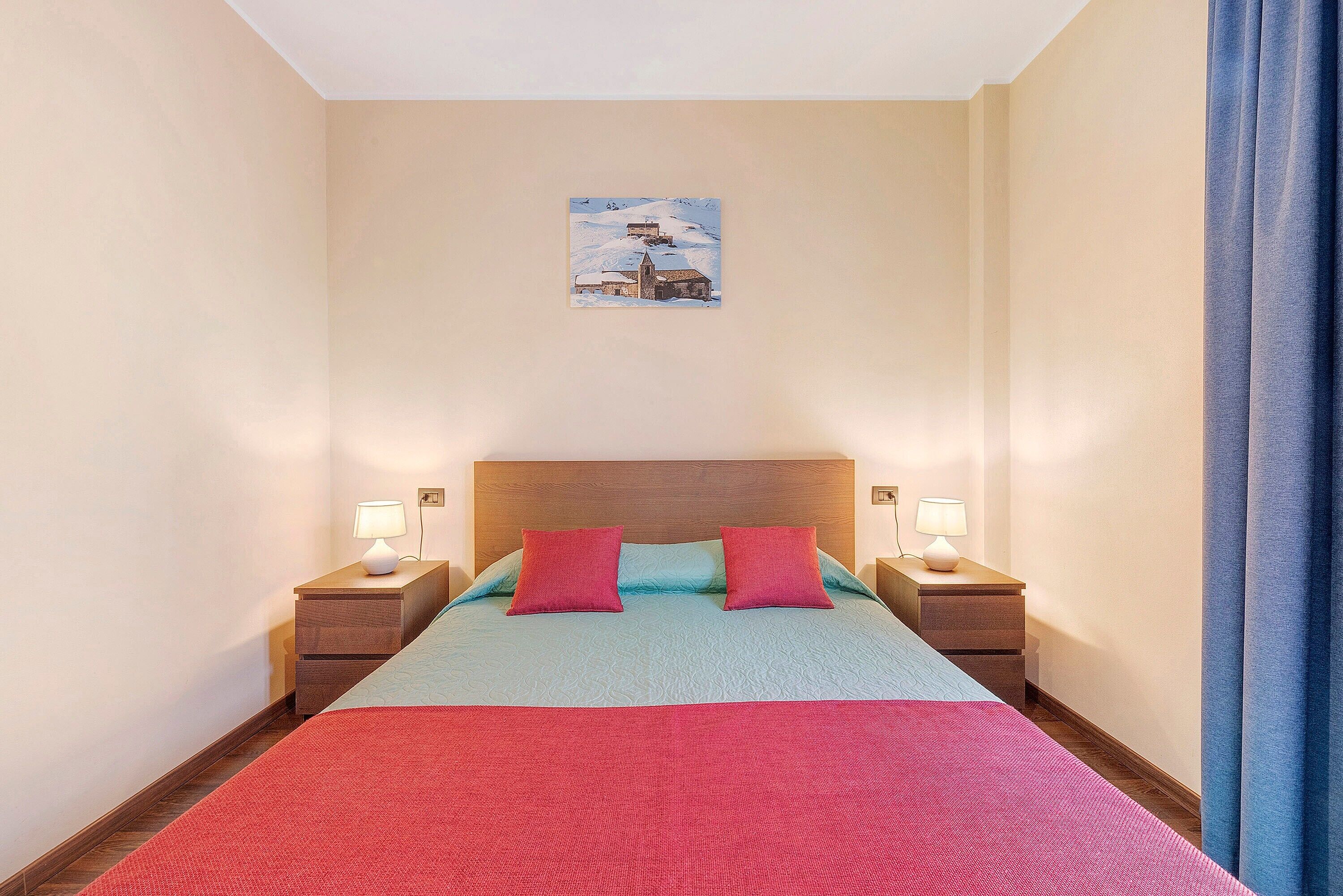 A bedroom with a bed, two nightstands, a headboard, a painting on the wall, and a window with curtains.