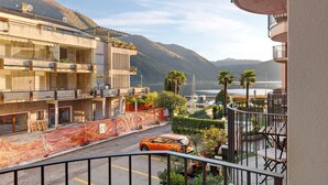 Un immeuble d’habitation doté de balcons, une rue avec une voiture, et des montagnes en arrière-plan.