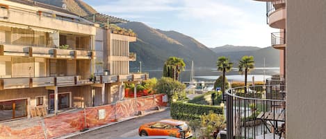 A residential building with balconies, a street with a car, and mountains in the background.