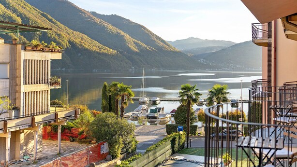 Un balcon avec vue sur un lac, des montagnes et des voitures garées.