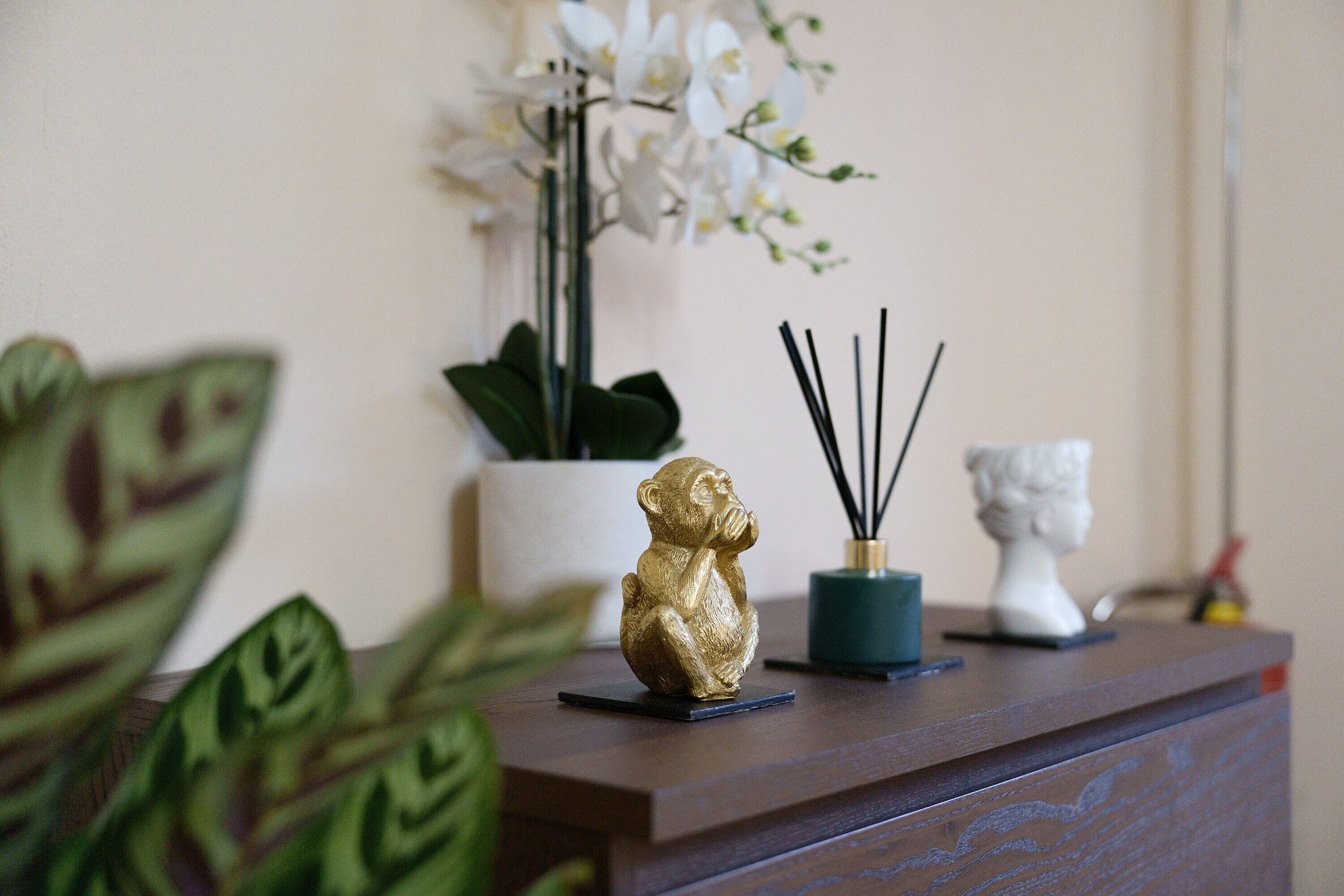 Ein Holztisch mit einer goldenen Figur, einer weißen Vase und einem blauen Behälter mit schwarzen Stöcken.